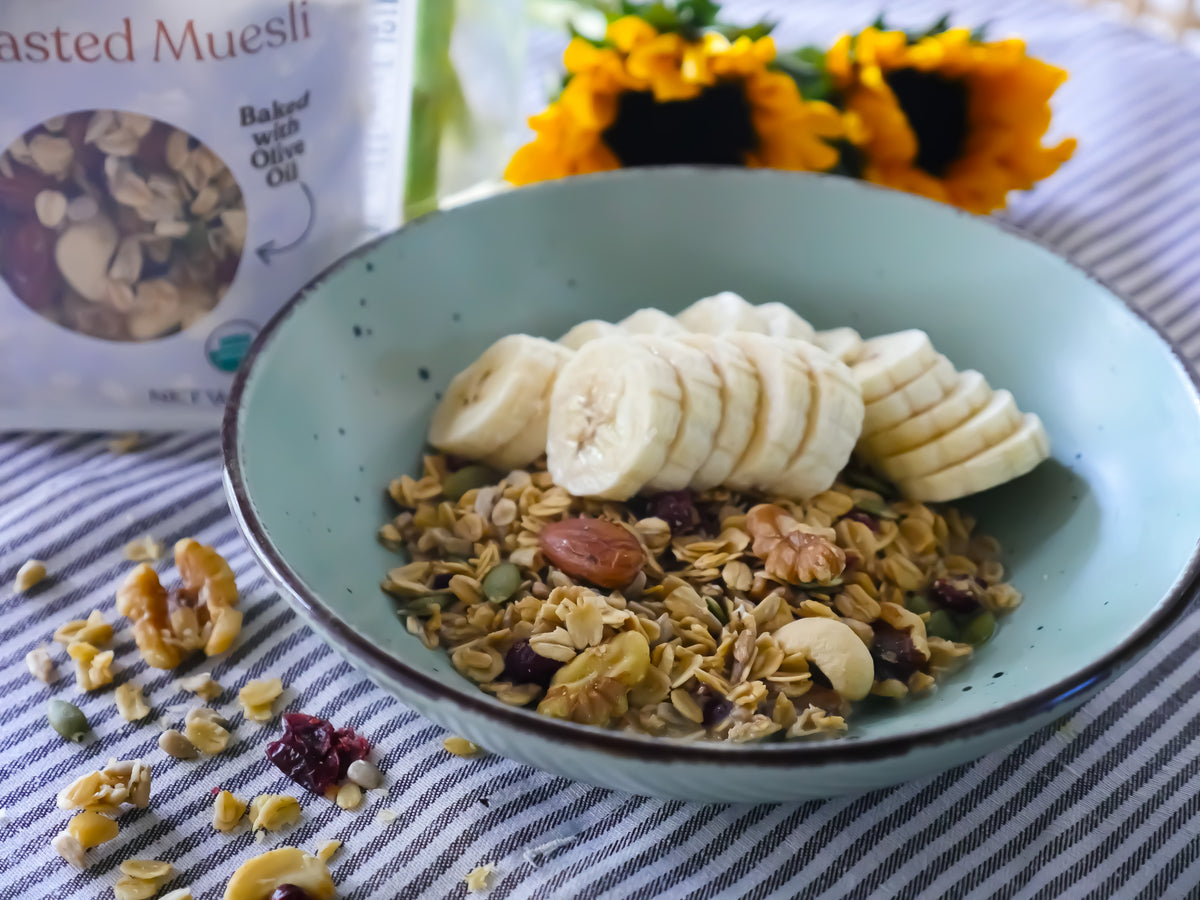 Bowl of muesli with sliced bananas on a striped tablecloth, with a pouch of muesli in the background.